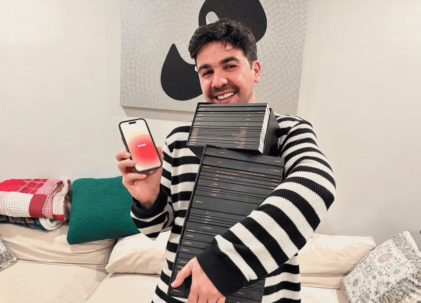 Artin Bogdanov holding a phone with the SUN app and a stack of Bible volumes